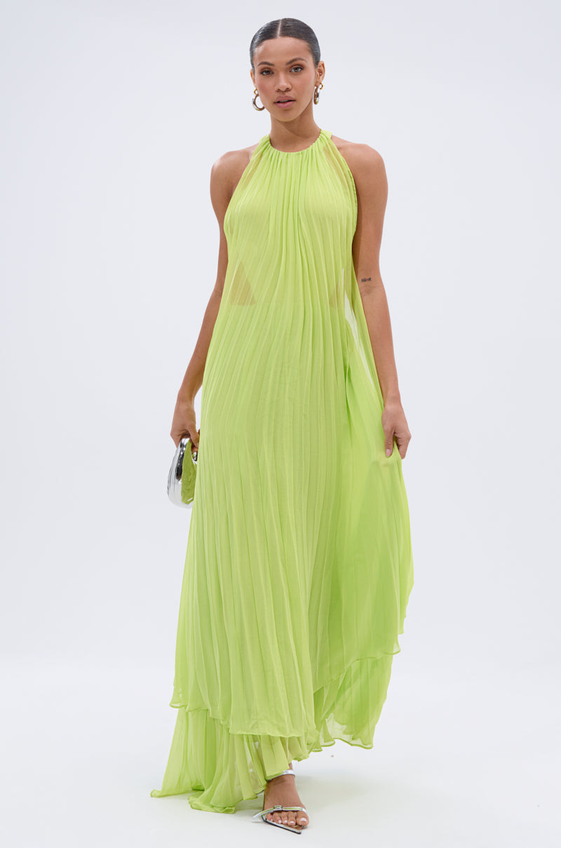 A woman in a neon green NIXEN MAXI DRESS WITH CHIFFON OVERLAY, styled with silver hoop earrings, silver heels, and a small silver clutch, poses against a plain white background.