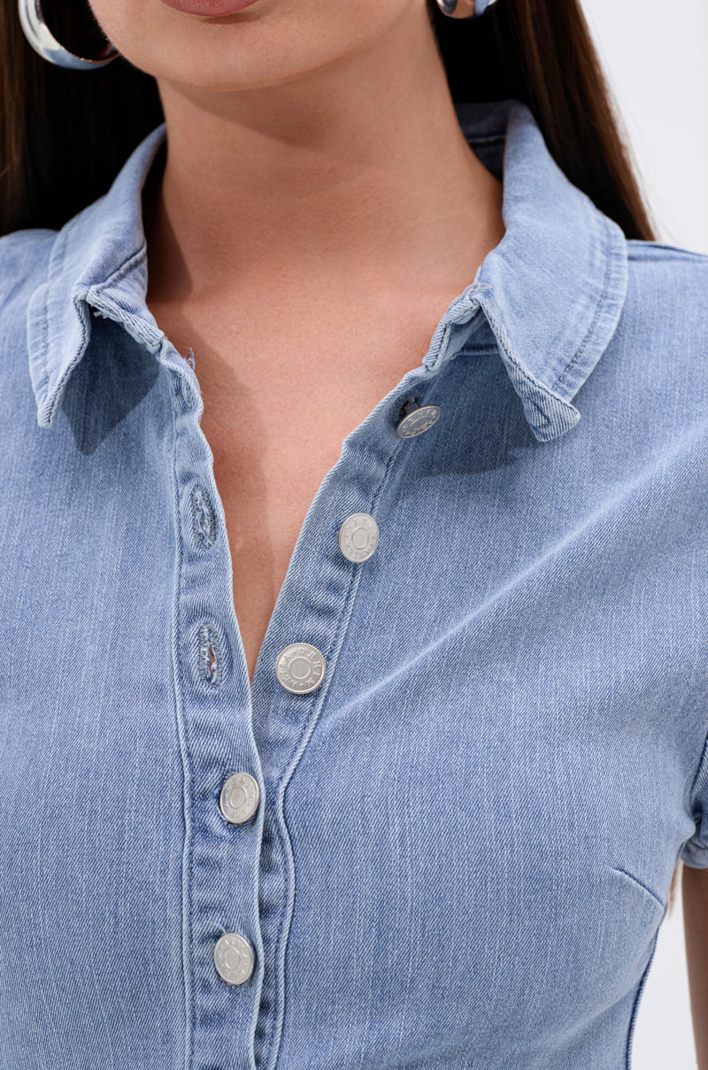 Close-up of a woman wearing the LEAVE IT RUFFLED JUMPSUIT IN DENIM, featuring silver buttons, an open collar, and large silver hoop earrings; only her lower face and upper torso are visible.