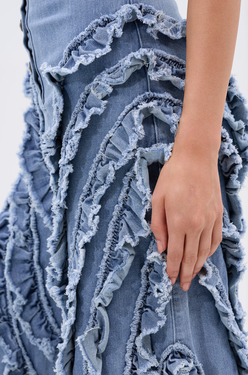 A close-up of a hand resting on the LEAVE IT RUFFLED JUMPSUIT IN DENIM, highlighting the frayed, ruffled spiral patterns and detailed denim texture.