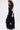 A woman with curly hair models the LEAVE IT RUFFLED JUMPSUIT IN BLACK, a fitted short-sleeve jumpsuit with dramatic ruffles and wide legs, paired with black platform shoes against a plain white background.
