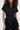 A woman with curly hair models the LEAVE IT RUFFLED JUMPSUIT IN BLACK, featuring gold buttons and ruffled side details. The cropped photo highlights its chic wide-leg silhouette from chest to mid-thigh.