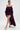 A woman walks confidently in gold platform heels, wearing ROYAL BLOOMER SHORTS in deep purple with ruffled details and a high-rise fit against a plain white background.