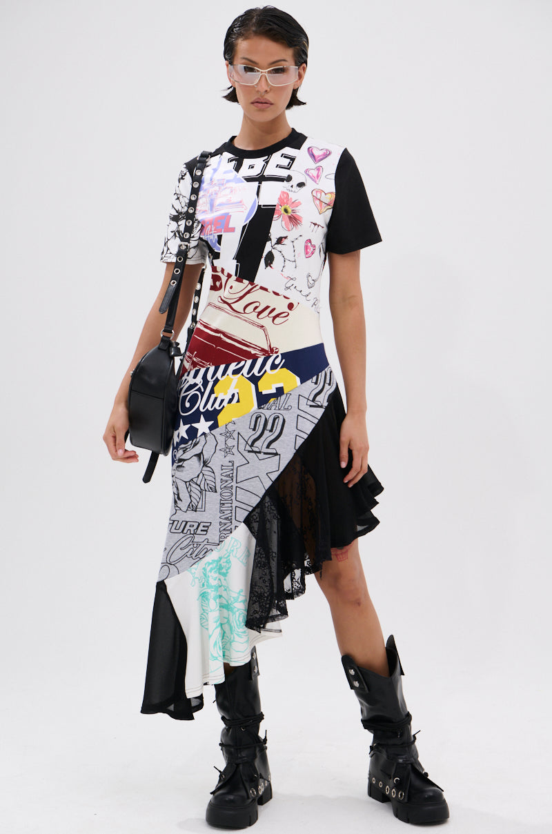 A person with short dark hair wears the YOU WERE THE ONE PATCHWORK MIDI DRESS with graphic prints and an asymmetrical hem, styled with black buckle boots, a black crossbody bag, and clear-frame glasses, standing confidently against a white background.