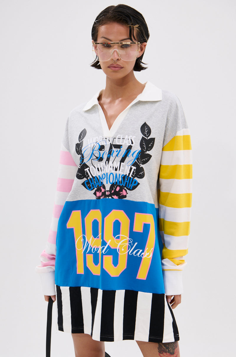 Wearing the HERE FOR THE DRINKS PRINTED TSHIRT DRESS, which features bold colorblock stripes, varsity graphics with "1997" in yellow, and printed text, a person stands against a plain background with wet hair and clear visor glasses.