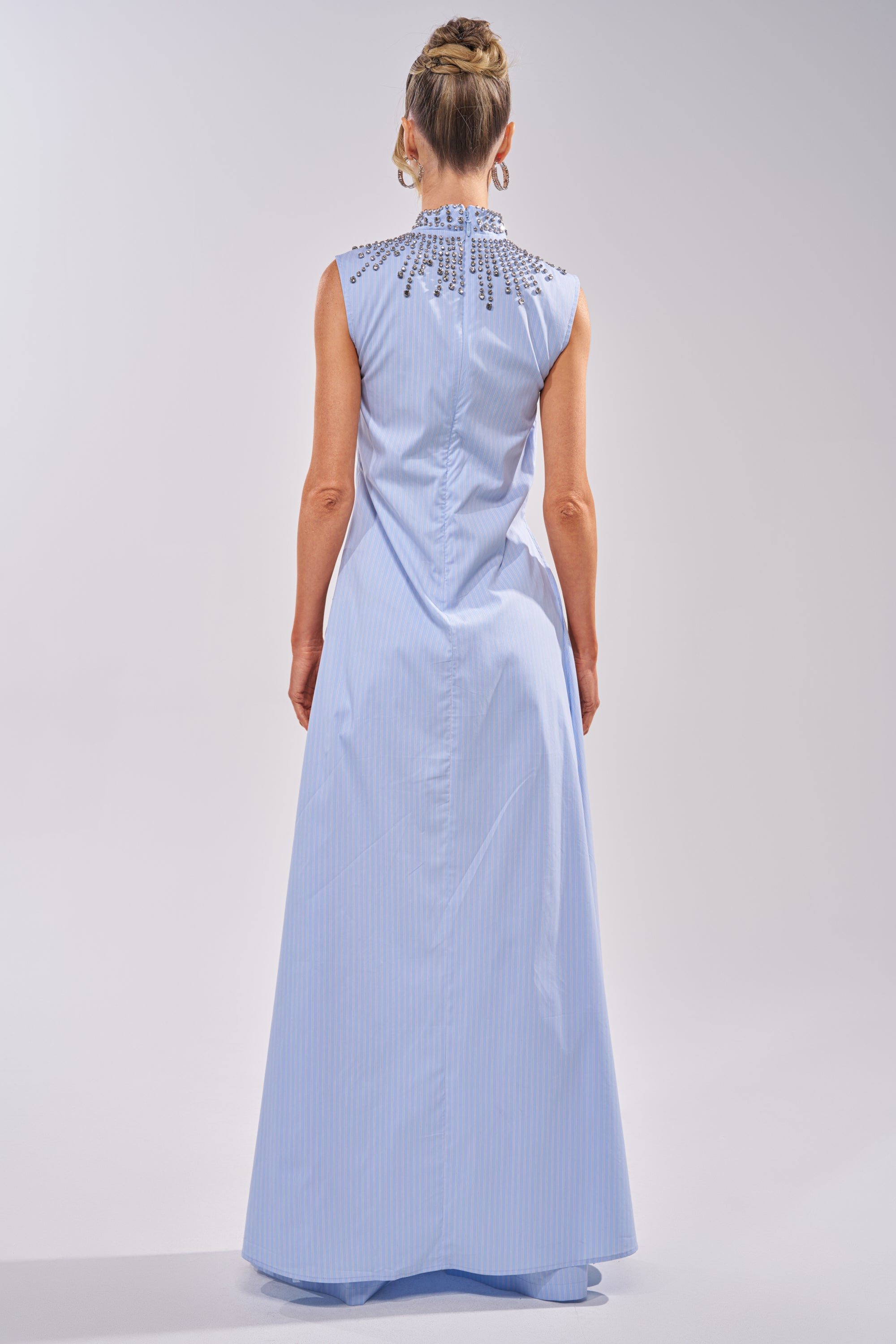 A woman stands facing away, wearing the STAR OF THE NIGHT POPLIN BLOUSE with decorative accents on the upper back and shoulders. Her hair is styled in a neat updo. 4