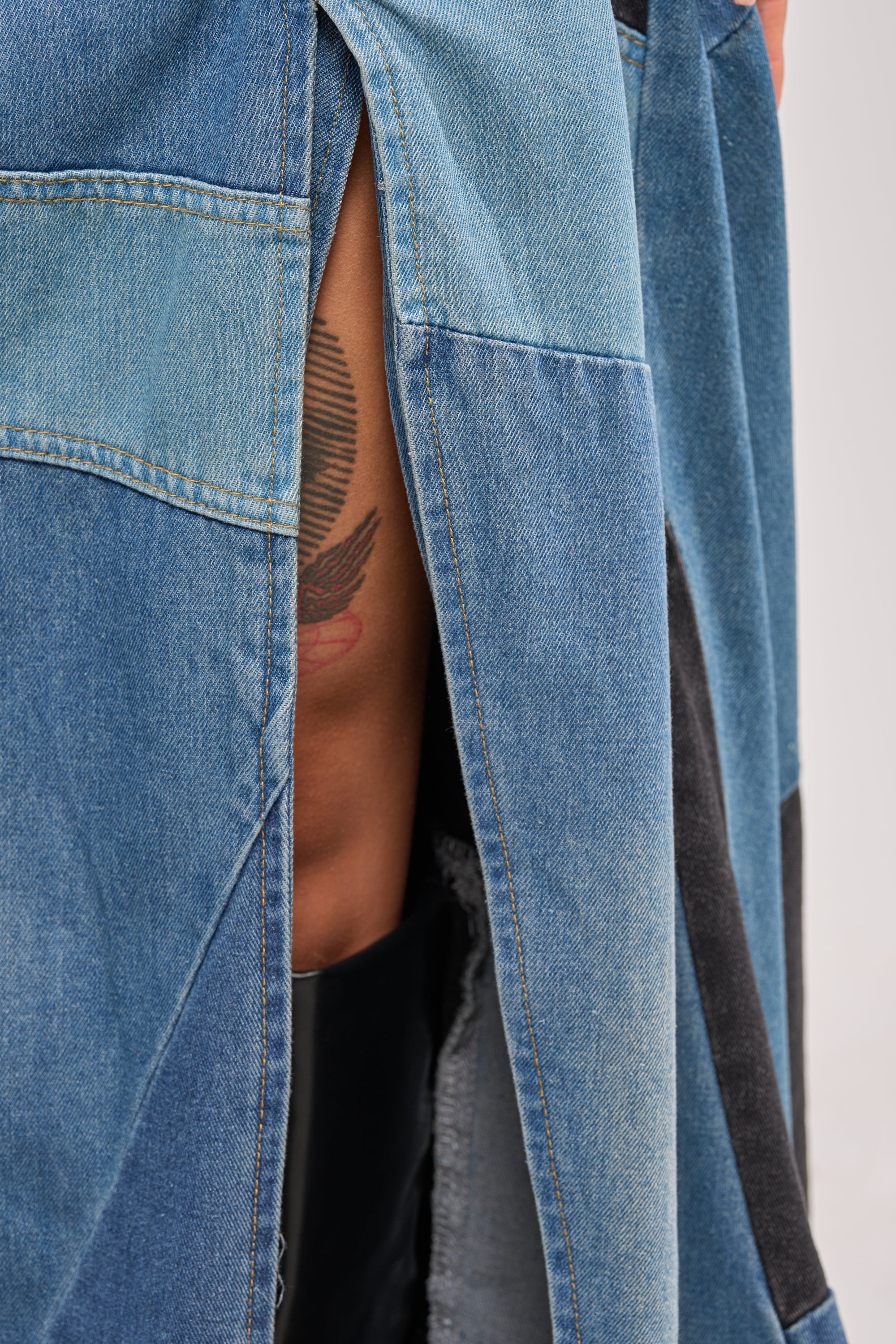 A close-up of a person wearing the LIFE IN DENIM STRAPLESS MAXI DRESS, a patchwork denim maxi with a high slit, revealing a bird tattoo on their thigh—an edgy reinterpretation of evening style. 6