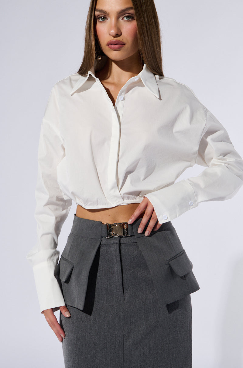 A person stands against a plain background wearing a white button-up shirt and a gray skirt with oversized pocket flaps. Their long, straight hair complements their neutral expression, accentuated by an air of confidence. The UTILTY CHIC BELT with a metallic silver buckle cinches their waist, adding subtle sophistication. 1