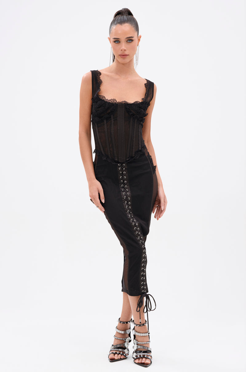 A woman stands against a white background wearing the LET ME REMIND YOU LACE UP MESH MIDI DRESS with a corset-inspired bodice and lace-up details, styled with strappy silver-embellished high heels and a sleek high ponytail.