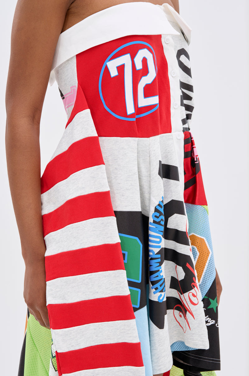 A person wears the STAND OUT GRAPHIC MINI DRESS, an off-the-shoulder mini with a white collar, red and white stripes, numbers, bold prints, and a flared skirt made from assorted jersey fabrics.