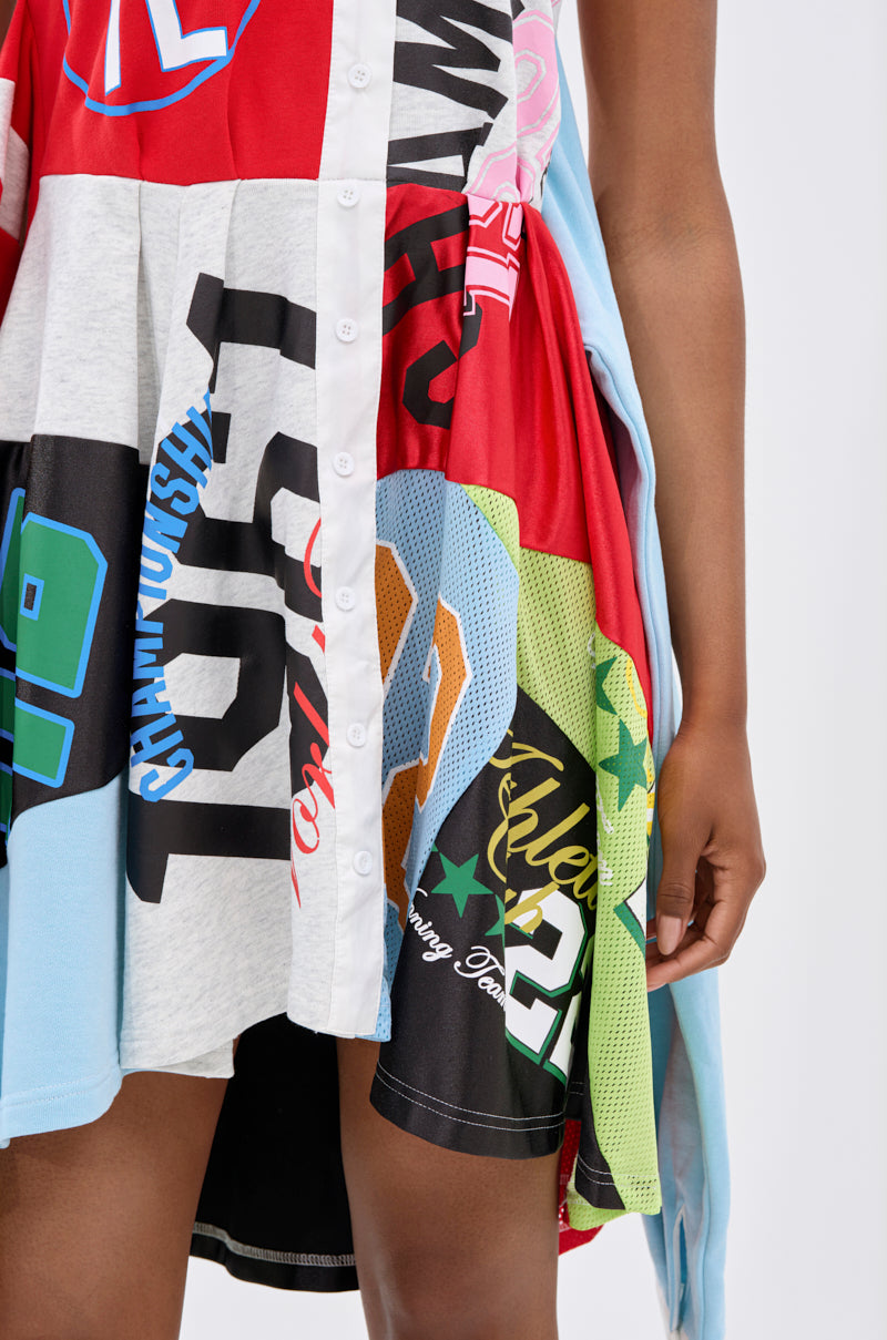 Wearing the STAND OUT GRAPHIC MINI DRESS, crafted from sports jerseys and graphic fabrics with front buttons, a person's lower torso and one arm are shown, highlighting this playful and vibrant mini dress style.