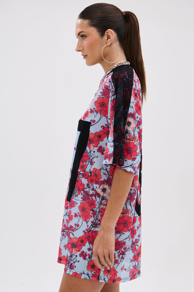 A woman with long brown hair in a ponytail models the POPPIN POPPIES LACE JERSEY DRESS, showcasing black lace shoulders and bold poppy print in a loose, short-sleeve silhouette against a plain background. 6