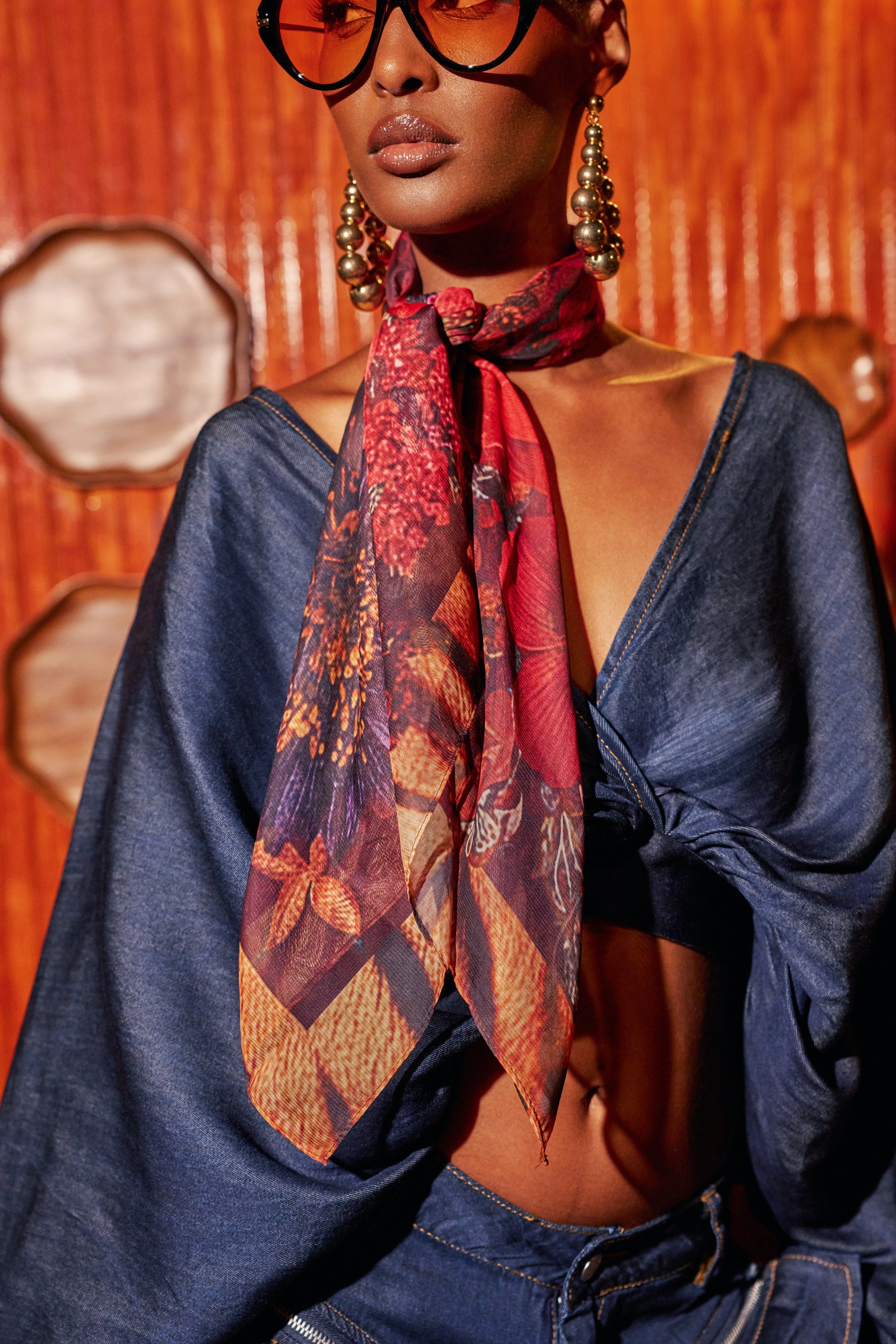 A person wears a red-toned, floral WILD FLOWER CHIFFON SCARF tied loosely around their neck in a festival styling.
