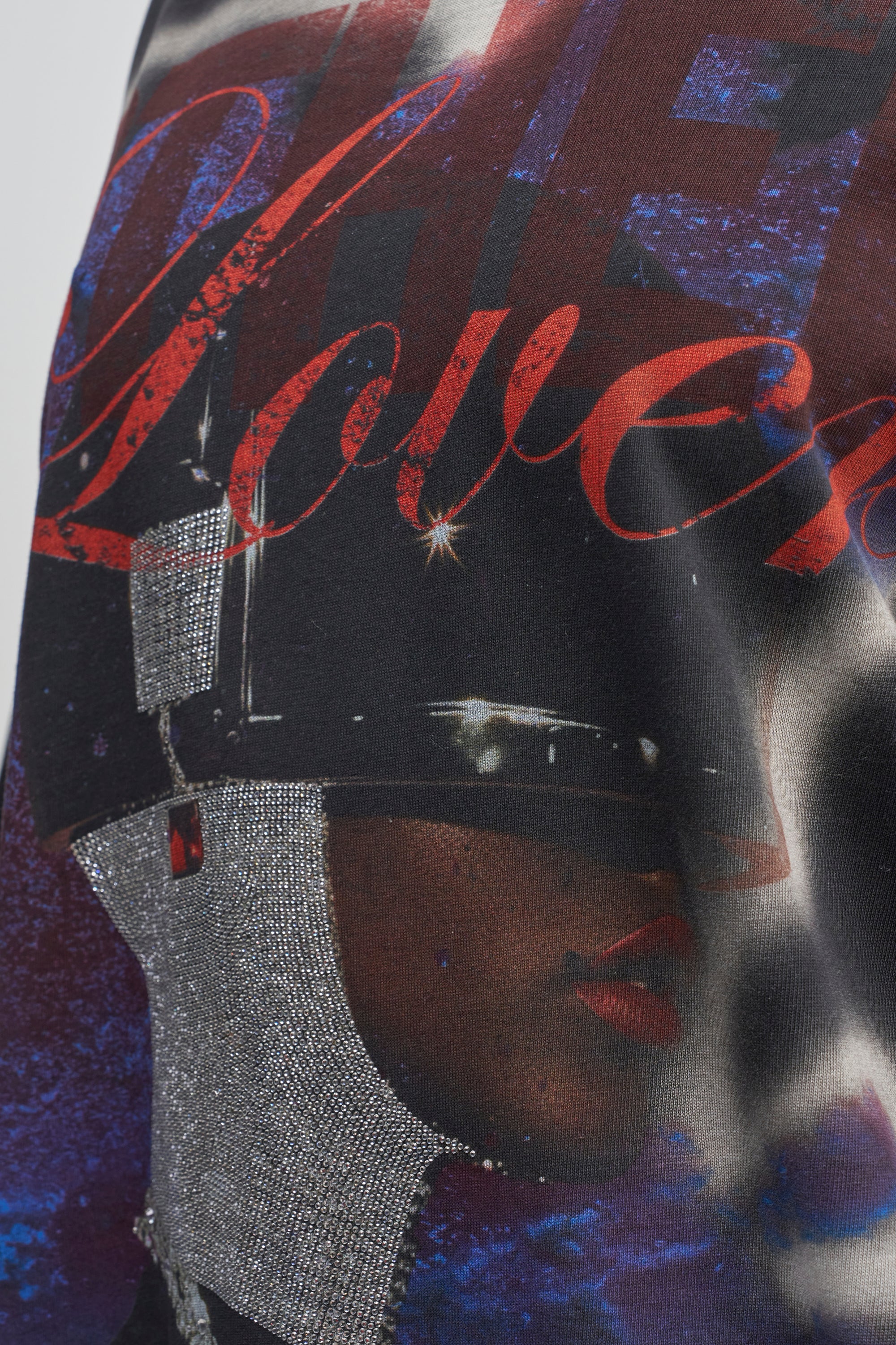 Close-up of fabric from the GIRLY BUT NOT LAYERED LACE MIDI DRESS IN BLACK MULTI, featuring a vibrant print with part of a face in a glittery silver helmet, red lipstick, and the word “Lover” scripted in red across a blue and black background—perfect for adding artistic flair to this eye-catching statement dress.