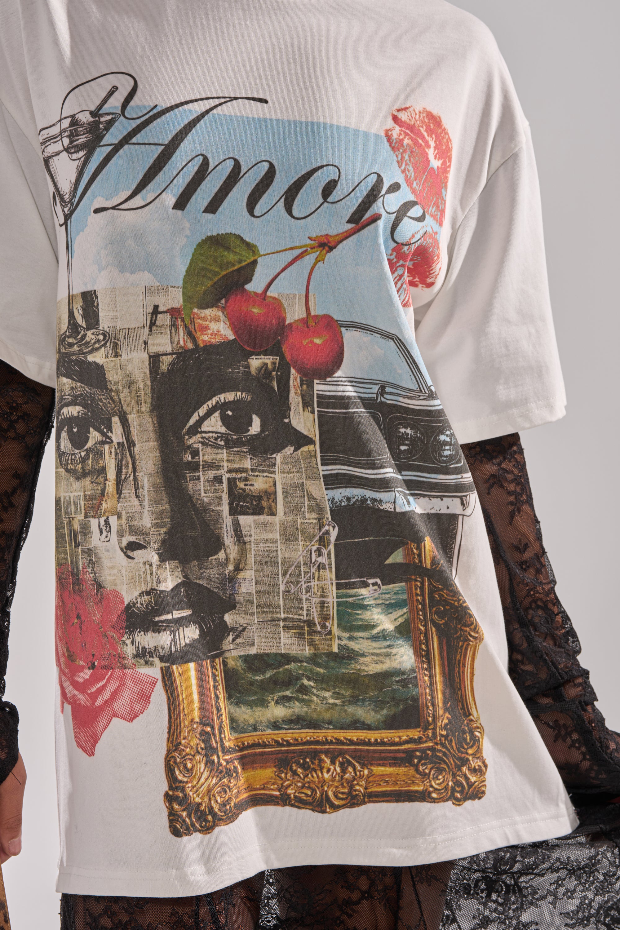 The GIRLY BUT NOT LAYERED LACE MIDI DRESS WITH GRAPHIC is styled over a white tee featuring a black-and-white face, red lips, cherries, and a vintage car collage, adding texture and contrast to the bold “Amore” graphic.