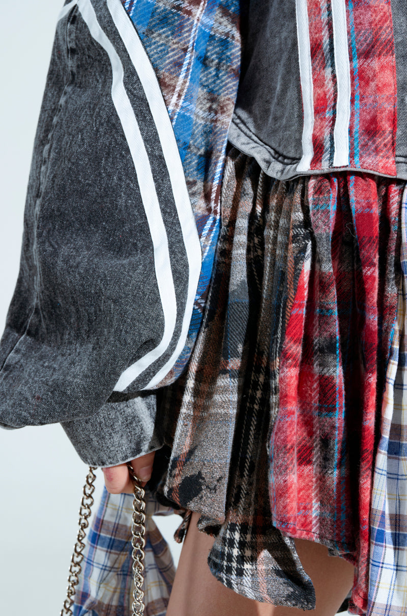 Close-up of someone in the A LITTLE BIT OF EVERYTHING PLAID SWEATSHIRT DRESS featuring vibrant red, blue, and gray patterns with frayed edges, paired with striped sleeves and an oversized fit while holding a small chain for an eclectic look.