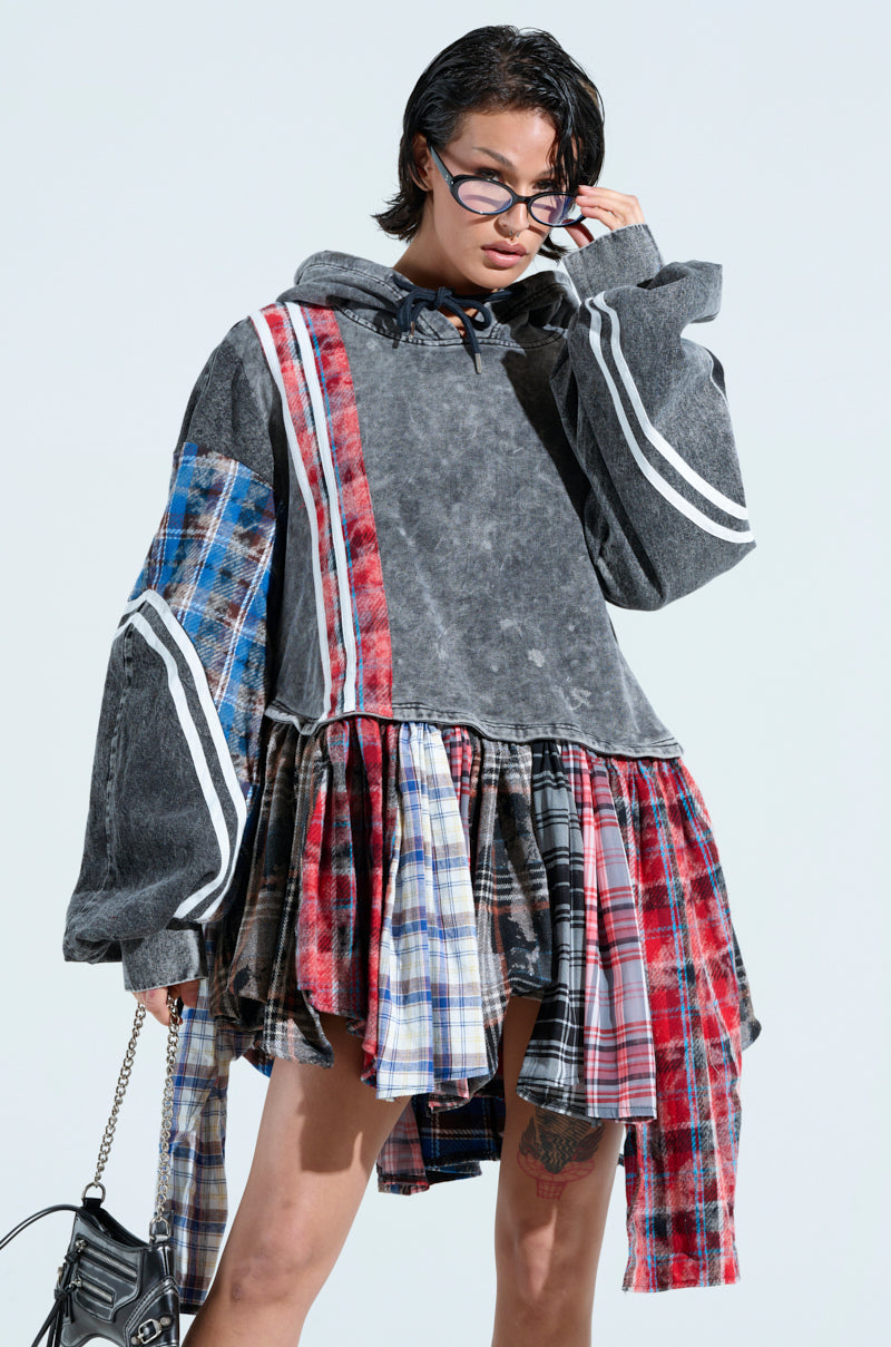 Dressed in the A LITTLE BIT OF EVERYTHING PLAID SWEATSHIRT DRESS, which combines cozy cotton with plaid and solid patterns, an individual embodies trendy comfort. The hooded, oversized fit's grand sleeves complement their short wet-look hair and glasses as they hold a chic handbag.