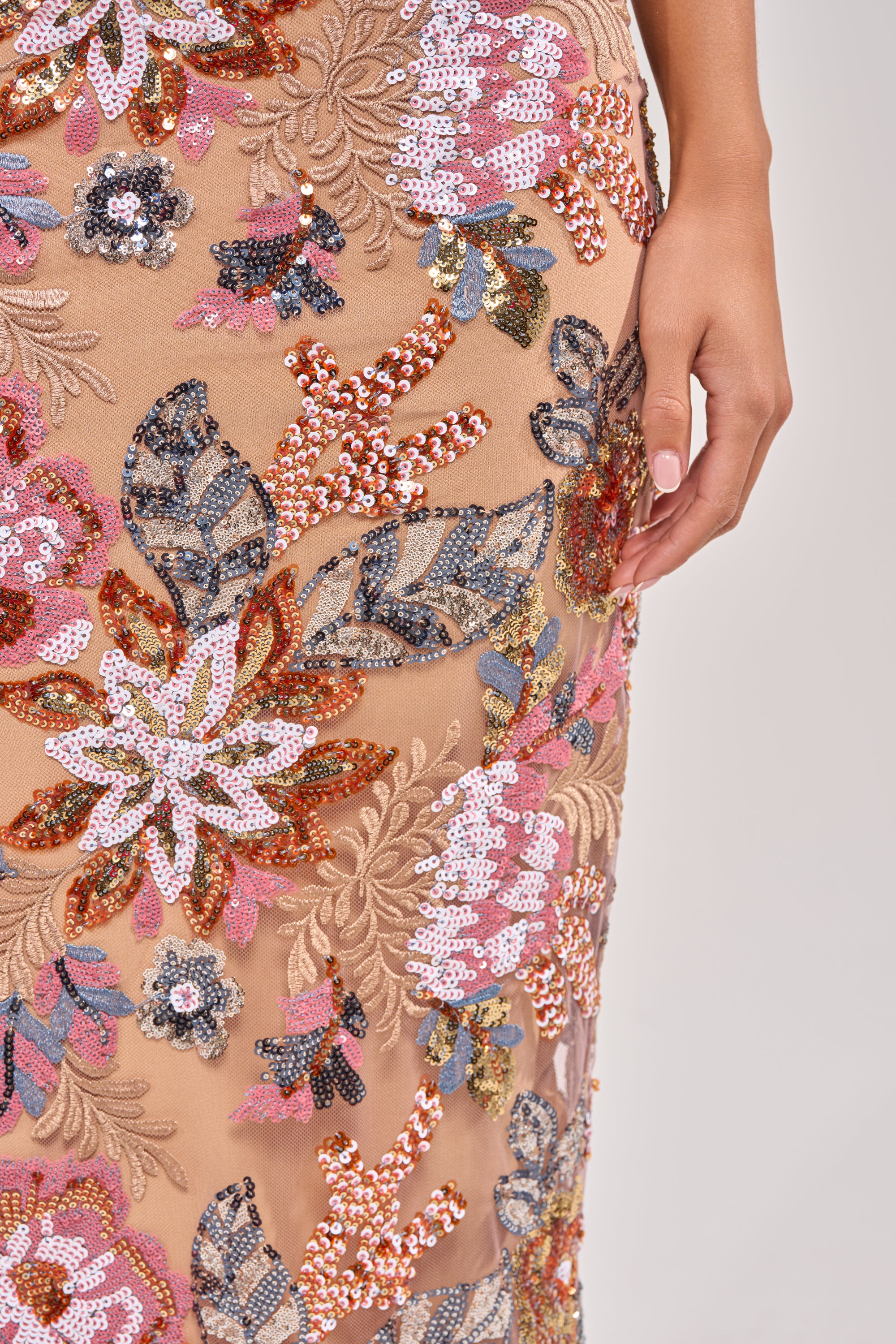 A close-up of a hand on the SHOW ME LOVE EMBELLISHED MIDI DRESS, featuring embroidered pink, orange, white, and blue flowers on sheer nude fabric—a strapless sequin midi that adds standout style to any occasion wardrobe. 5