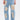 A person wears ROYAL ENERGY BROCADE PATCH RELAXED DENIM—light-wash jeans featuring large rectangular beige brocade patches on the front, raw hems, and paired with a cropped top.