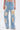 A person wears ROYAL ENERGY BROCADE PATCH RELAXED DENIM—light-wash jeans featuring large rectangular beige brocade patches on the front, raw hems, and paired with a cropped top.