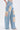A person wearing ROYAL ENERGY BROCADE PATCH RELAXED DENIM featuring light-wash, wide-leg jeans with large cream brocade patches on the front and sides. Only the lower torso and legs are shown against a plain background.