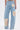 A person wearing ROYAL ENERGY BROCADE PATCH RELAXED DENIM—light-wash, wide-leg jeans featuring bold brocade patches on the back pocket, left thigh, and right calf—stands against a white background.