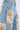 Close-up of ROYAL ENERGY BROCADE PATCH RELAXED DENIM, light-wash jeans with large cream, gold, and pink brocade patches on legs and pockets; frayed edges add a vintage, handmade touch.