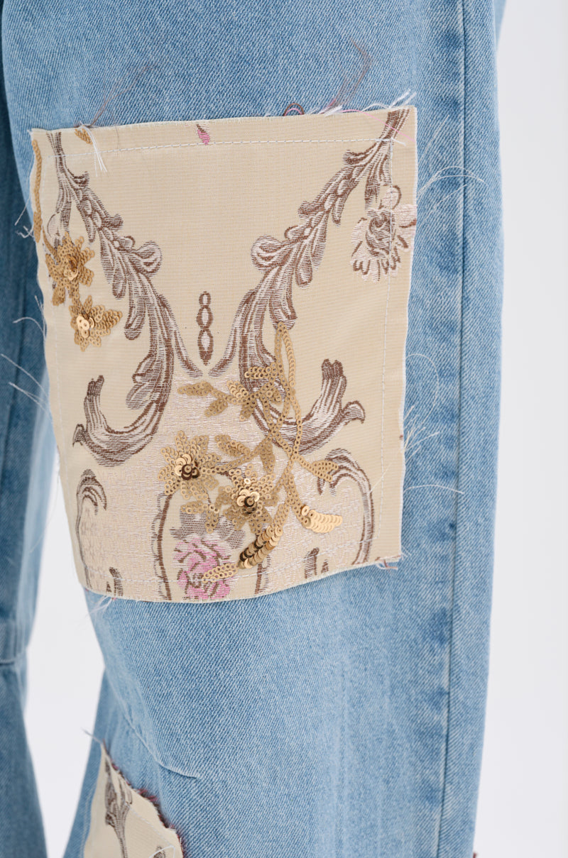 Close-up of blue denim with a beige brocade patch, detailed embroidery, and slight fraying—perfect for elevating your ROYAL ENERGY BROCADE PATCH RELAXED DENIM or pairing with light-wash jeans.