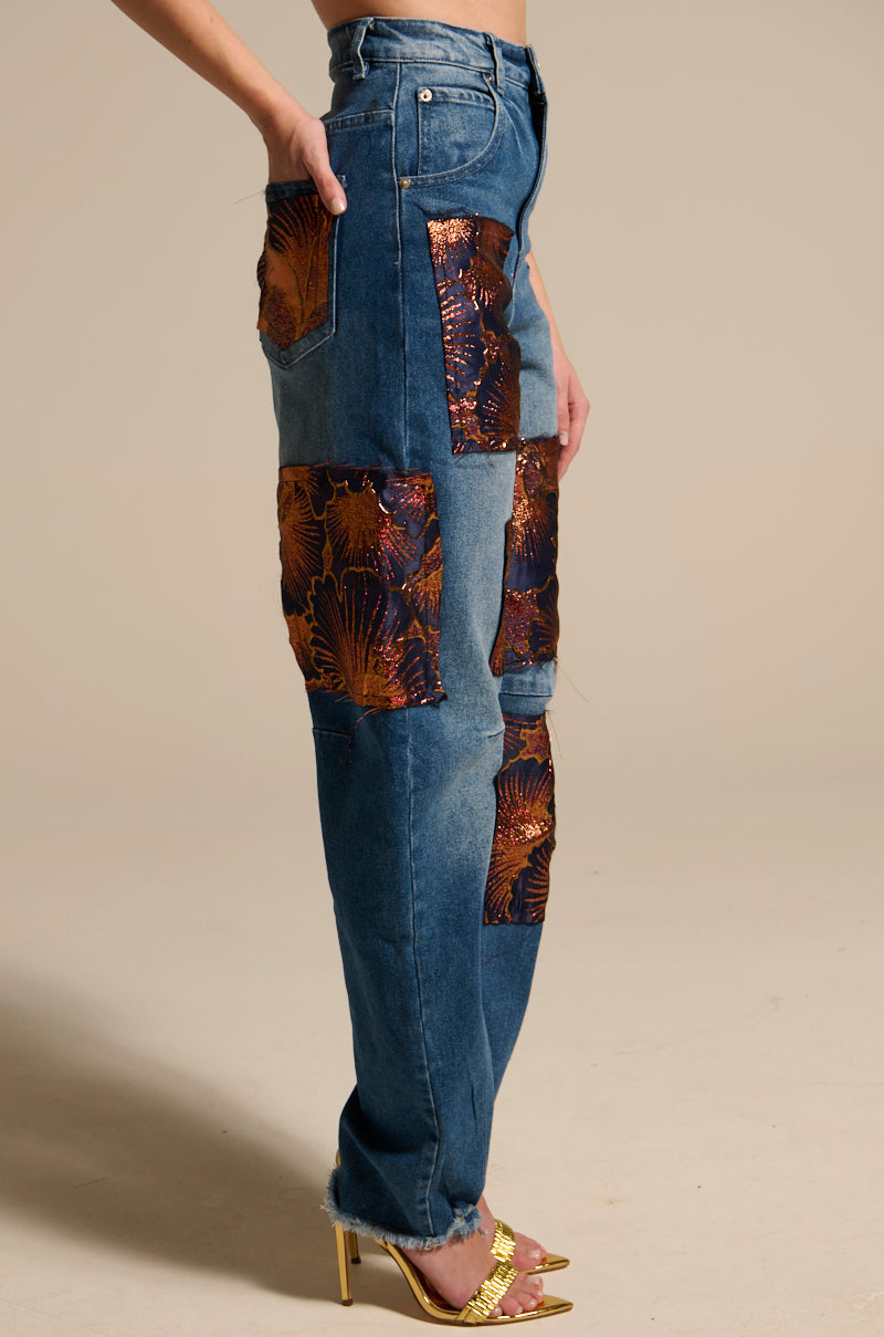 A person models the ELEGANT VIBES BROCADE PATCH RELAXED DENIM, featuring shiny metallic orange and brown shell-patterned patches, styled with gold high-heeled sandals. The side photo highlights the denim’s unique brocade design.