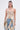 A woman wears the ROYAL ENERGY BROCADE CORSET TOP, featuring a vintage-inspired floral print, paired with high-waisted blue jeans with floral fabric panels and large bows. She has long straight hair and statement earrings against a plain white background.