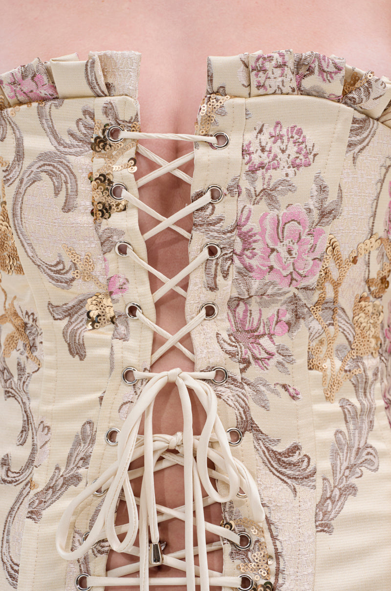Close-up of the ROYAL ENERGY BROCADE CORSET TOP in cream, featuring a vintage-inspired floral print with gold sequins, silver accents, and satin brocade lacing that reveals skin between the cream cords.