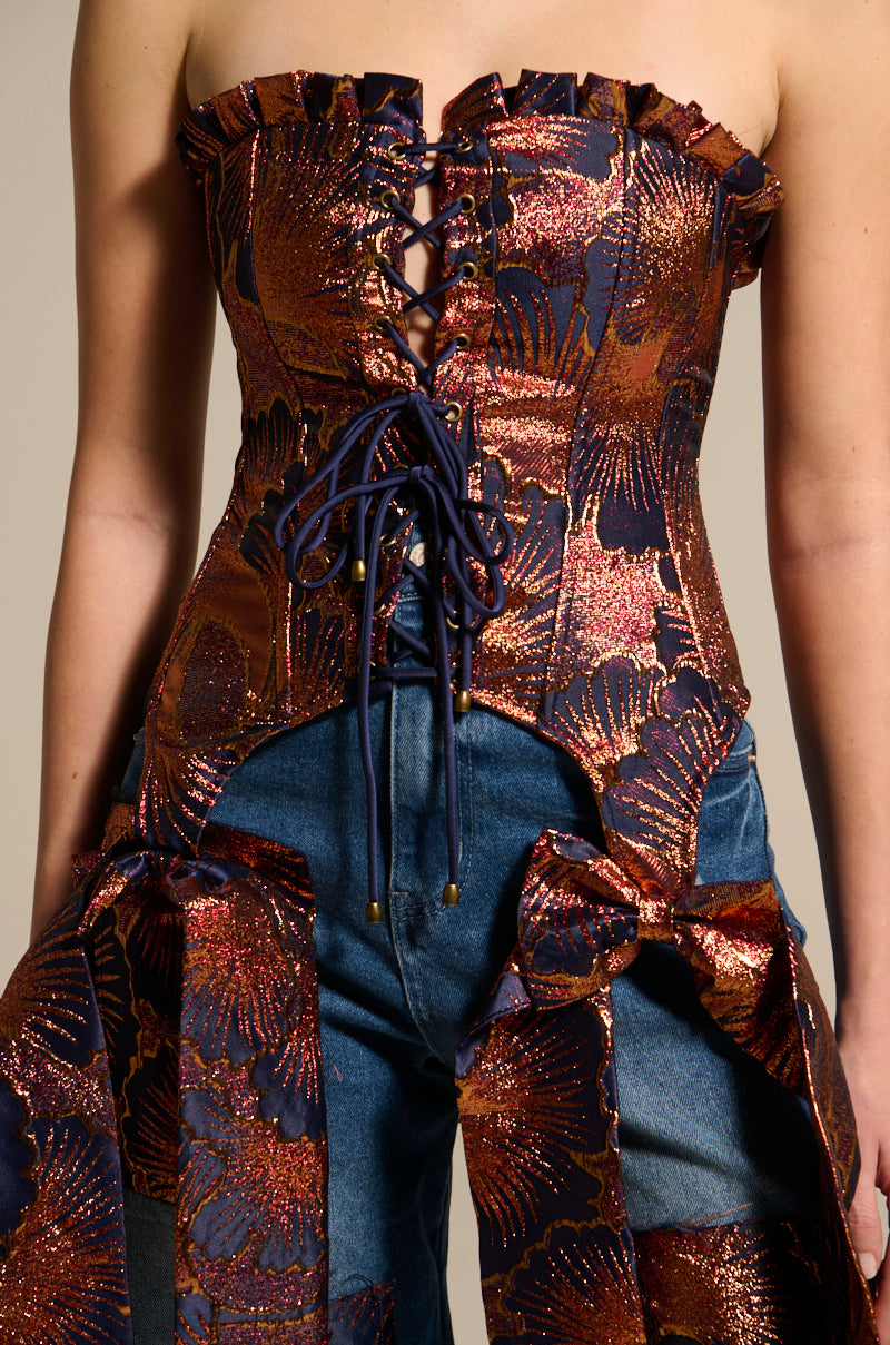 Wearing the ELEGANT VIBES BROCADE CORSET TOP in navy and copper with metallic floral motifs, paired with blue jeans featuring matching brocade fabric bows on the hips.