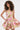 A woman with curly hair poses against a plain background wearing the PRETTY IN PINK BROCADE MINI DRESS—strapless, with a pink, gold, and white floral pattern and a flared ruffled mini skirt.