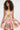 A woman with curly hair models the PRETTY IN PINK BROCADE MINI DRESS, which features a strapless neckline, flared skirt, and shiny pink, gold, and green floral brocade. She stands against a plain white background.