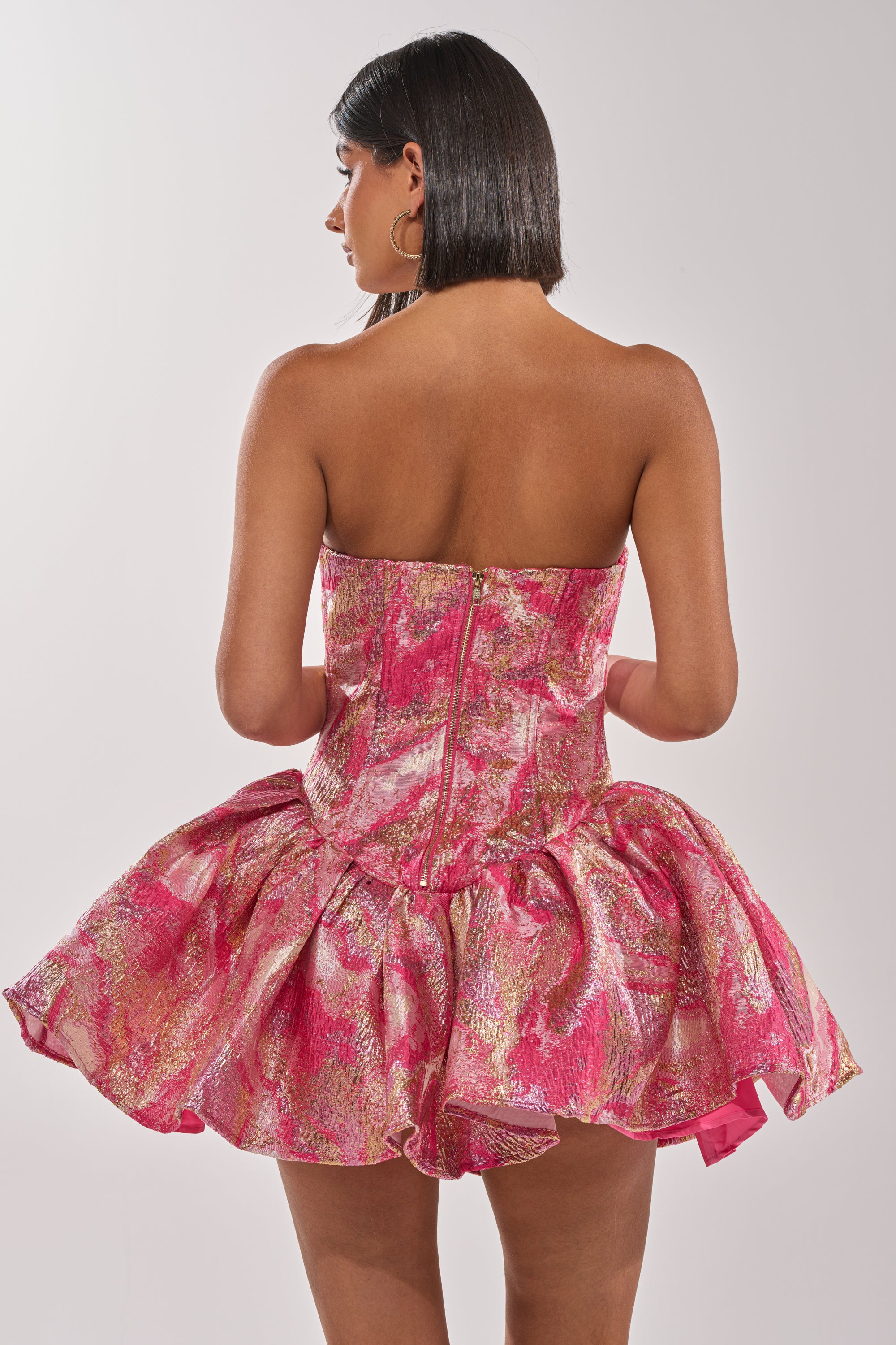 A woman stands gracefully in the PRETTY IN PINK BROCADE MINI DRESS IN PINK MULTI, its corset-style bodice accentuating her silhouette. 6