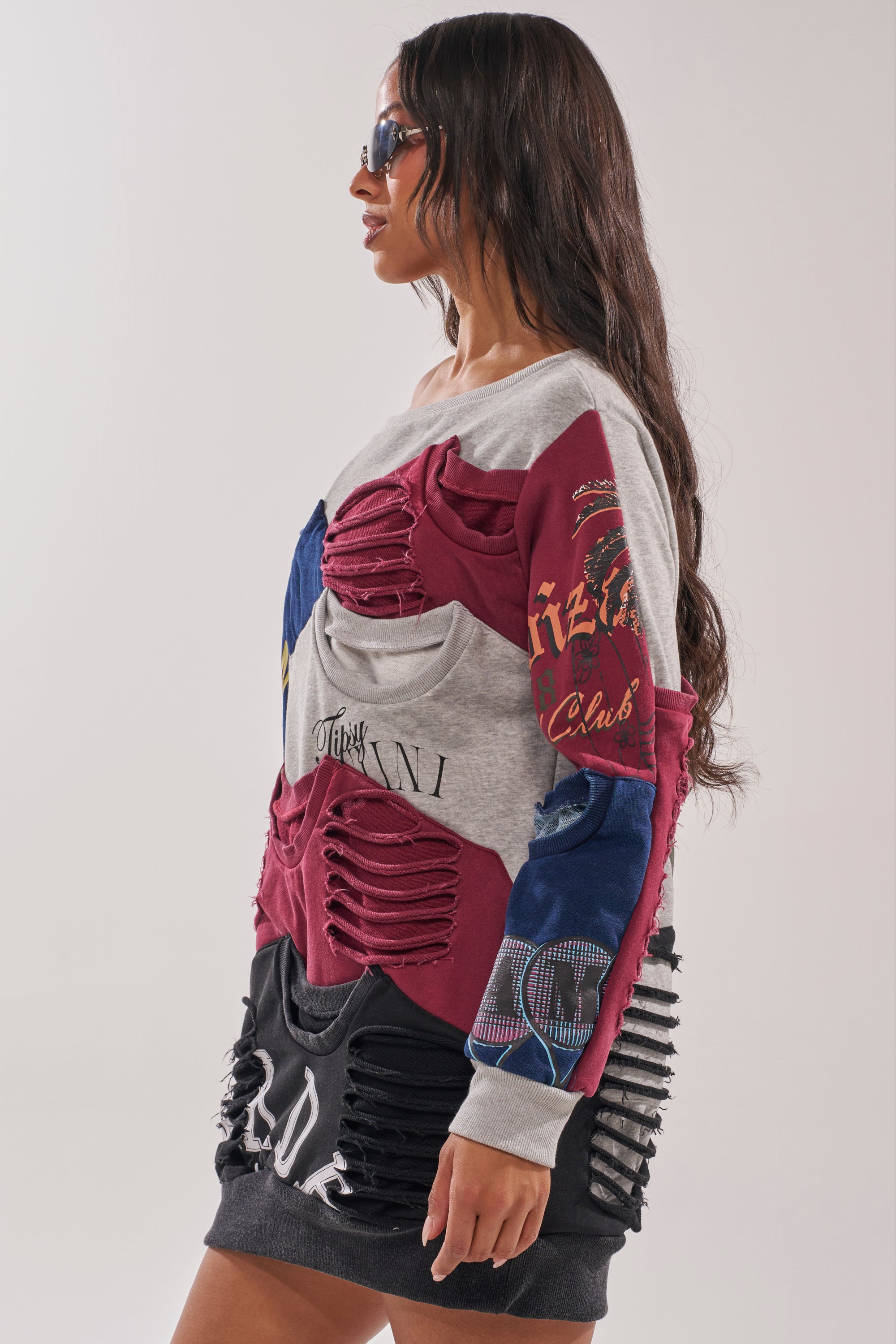 A woman in sunglasses models the TALK LATER OFF THE SHOULDER PATCHWORK DRESS—a street style look with shredded, cut-out sections in red, gray, blue, and black—standing in profile against a plain background. 2