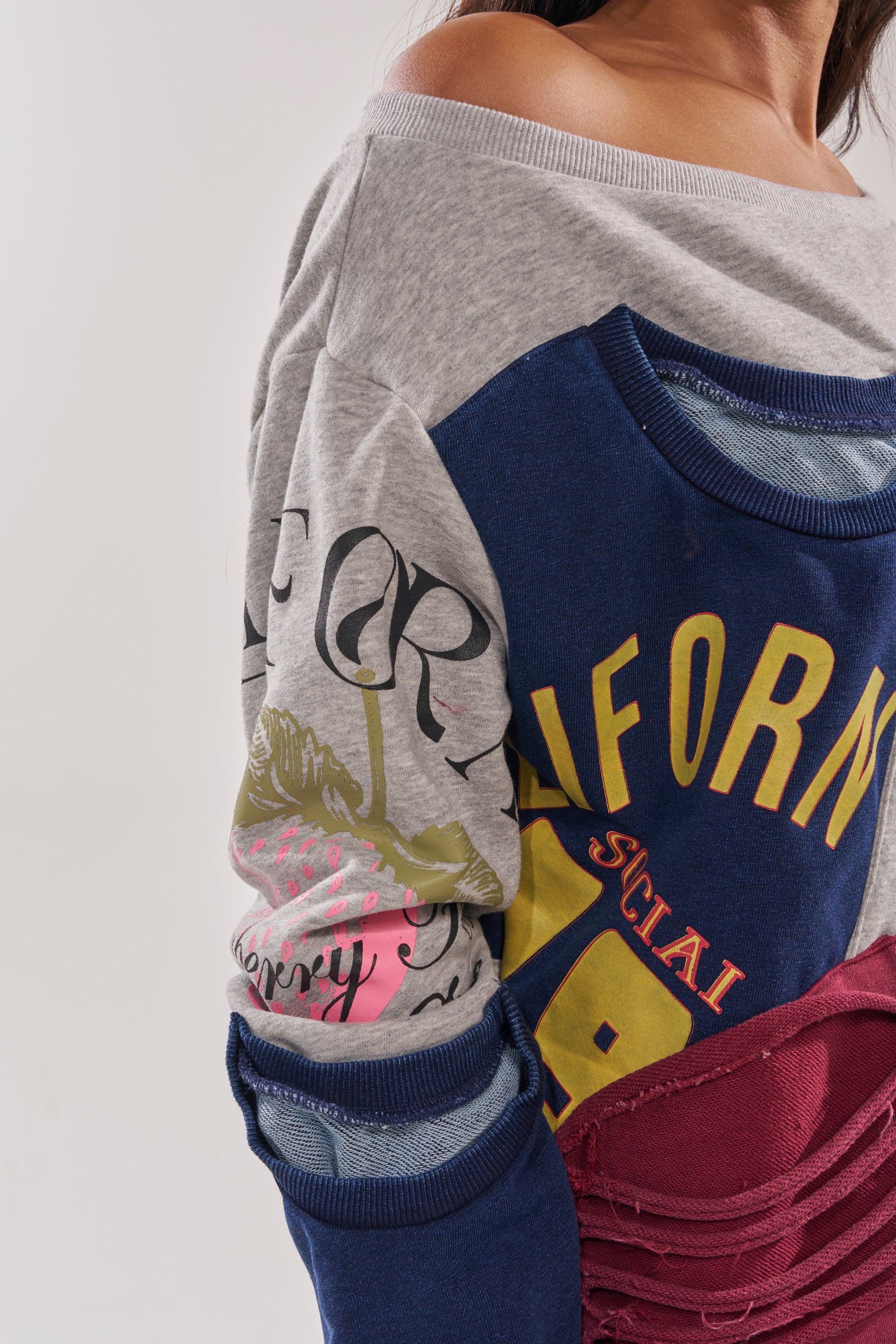 A person wears the TALK LATER OFF THE SHOULDER PATCHWORK DRESS—an oversized, color-blocked sweatshirt dress with printed designs and text. Only the upper torso and part of one arm are visible. 7