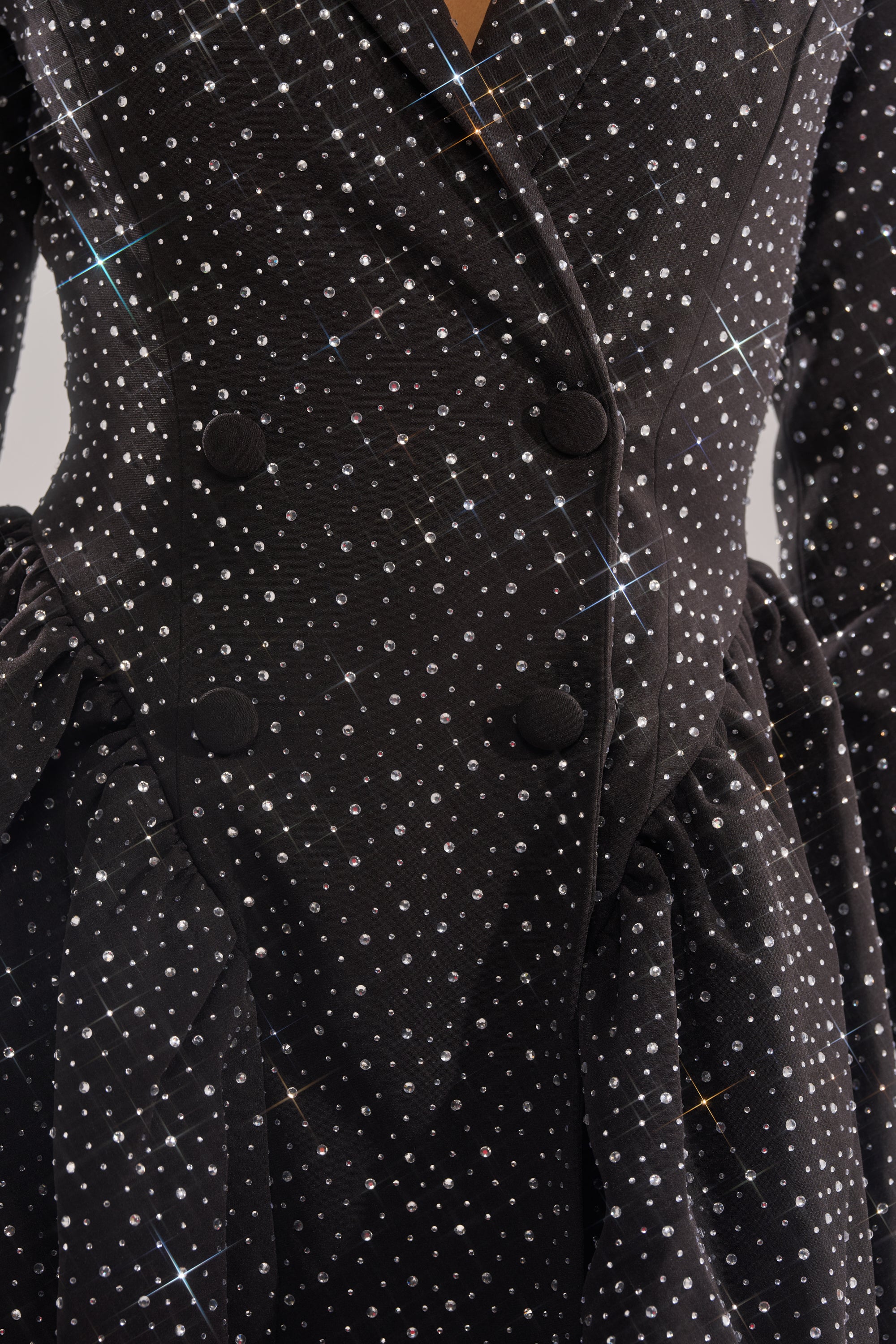 Close-up of the BACK IN BIZ MINI BLAZER DRESS by AKIRA Label, a black mini blazer dress with sparkling rhinestone embellishments, large black buttons, ruched waist detailing, and a shimmering fabric finish.