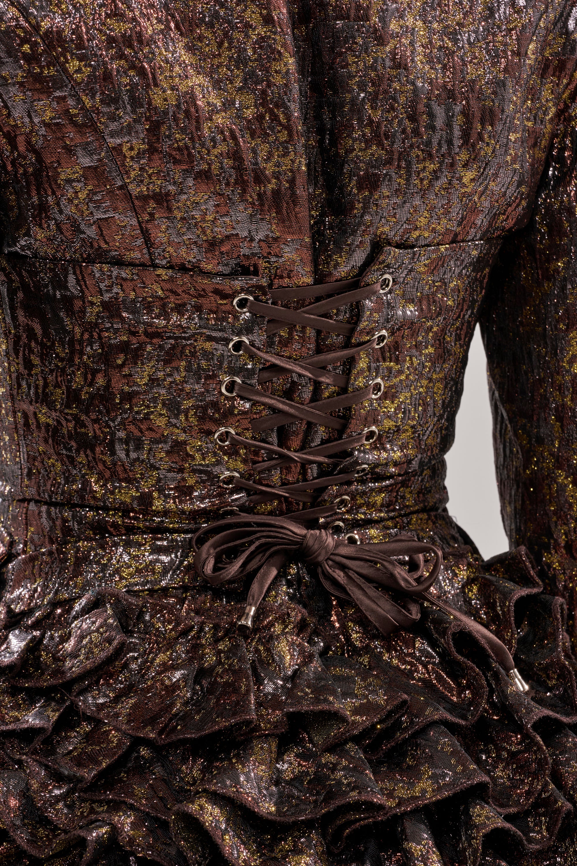 Close-up of the DANCING QUEEN BRONZE BLAZER ROMPER, featuring metallic textured brown and gold fabric with a corset-style lace-up back and ruffled details at the waist.