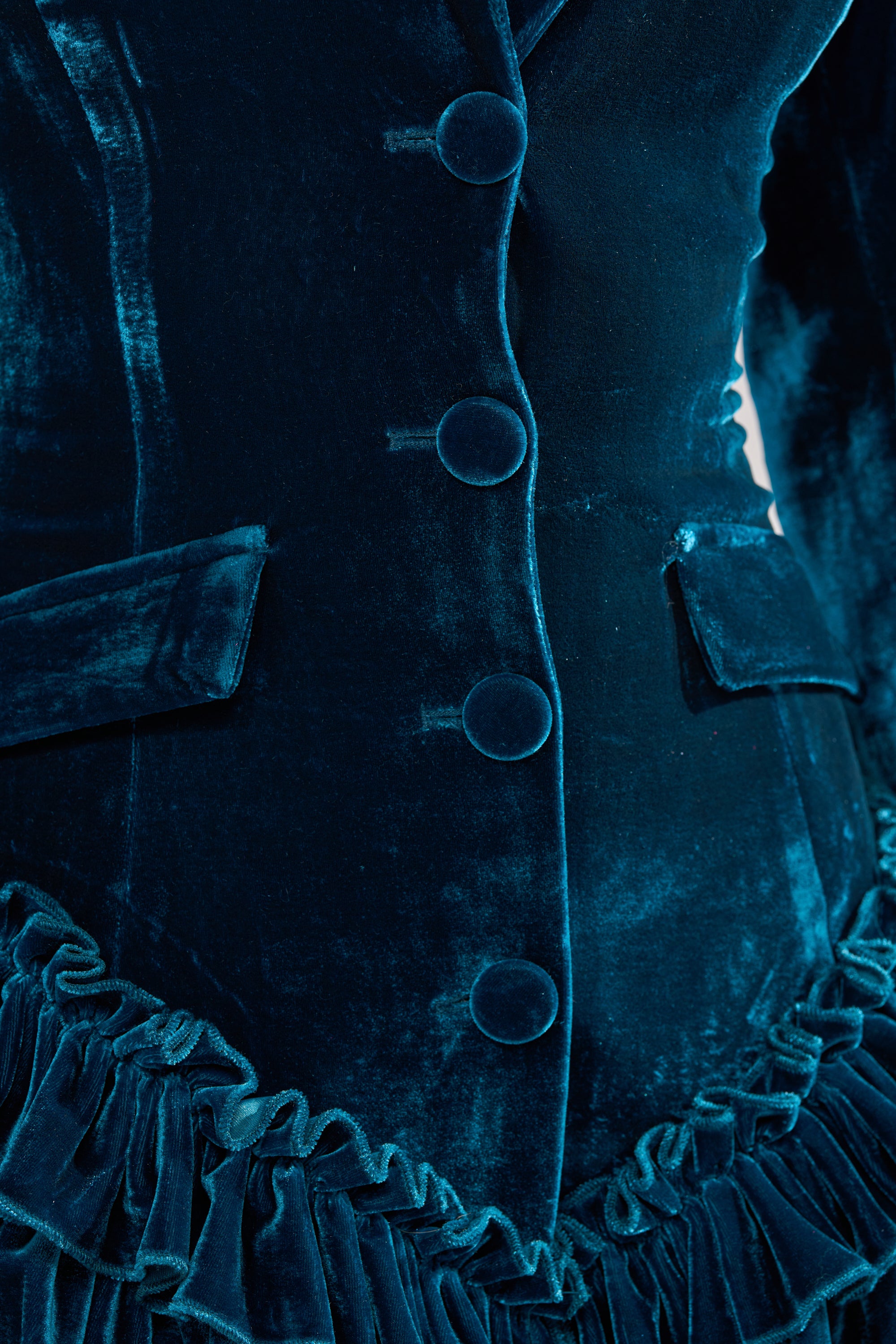 Close-up of the SHE'S ROYALTY VELVET ROMPER in teal crushed velvet, featuring covered buttons, flap pockets, a ruffle hemline, and a soft, rich texture with visible highlights and shadows.