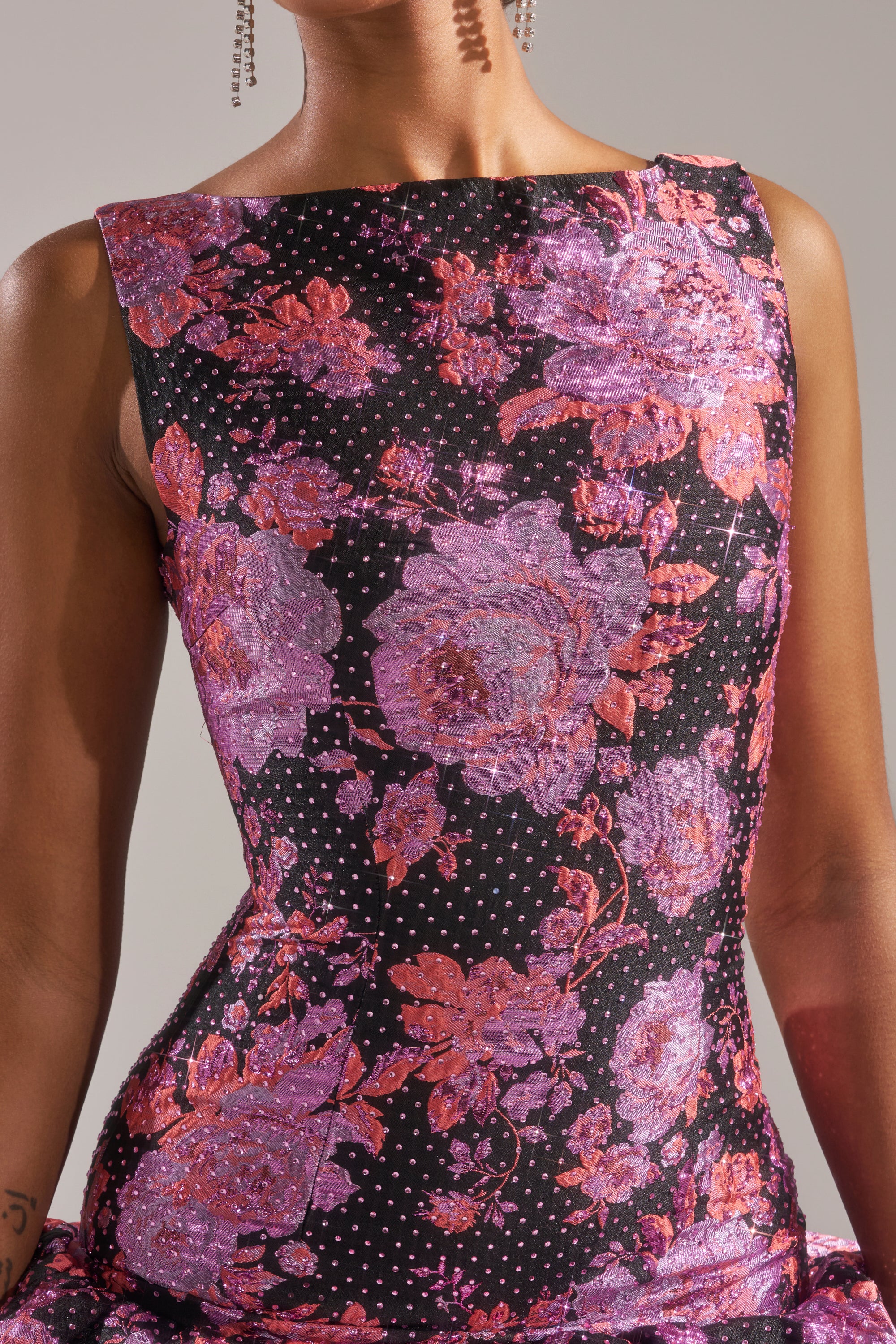 A person wearing the GIRLS WHO BRUNCH BROCADE MINI DRESS, a sleeveless black dress with pink and purple floral jacquard and white dots, stands against a neutral background. Only their torso and part of their arms are visible. 7