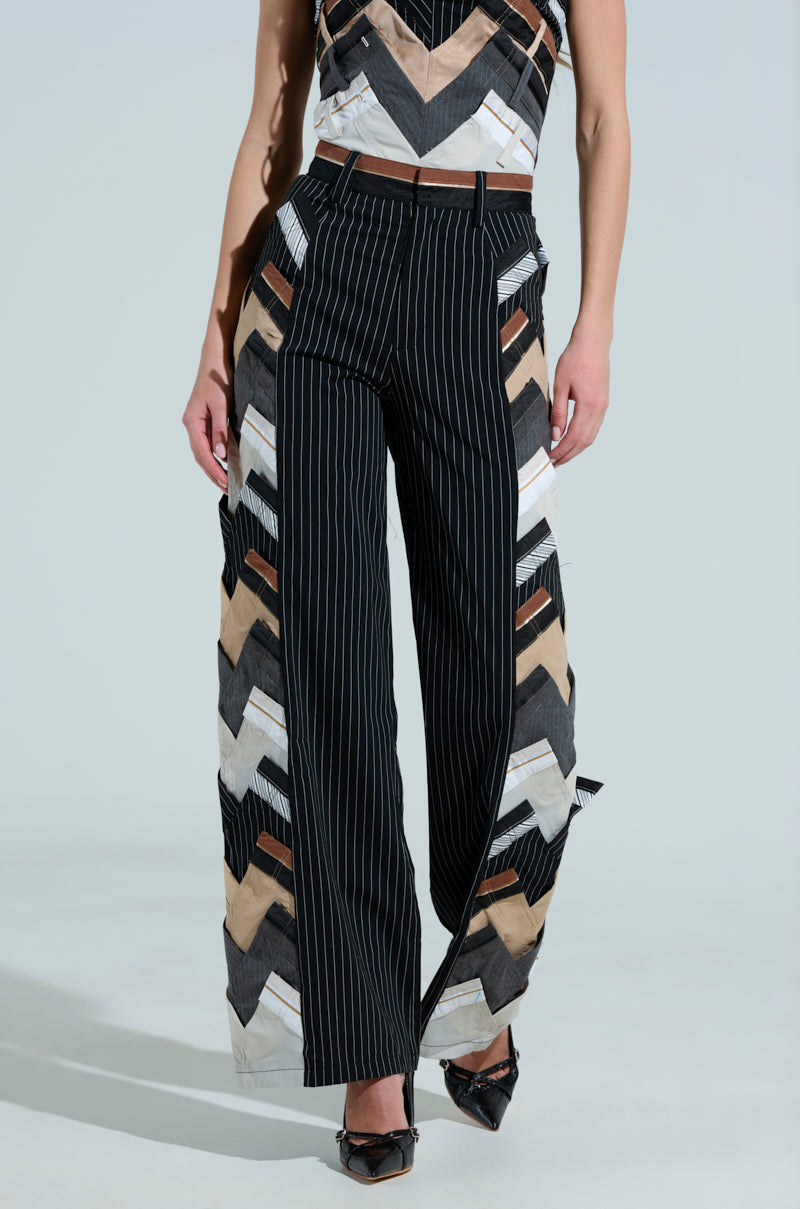 Dressed in a sleeveless top and STANDING ON BUSINESS LAYERED TROUSER, the ensemble features black, white, and beige with wide legs and chevron pattern. The pinstripe design on the front and open sides reveal layered fabric beneath, offering a sophisticated business-casual style.