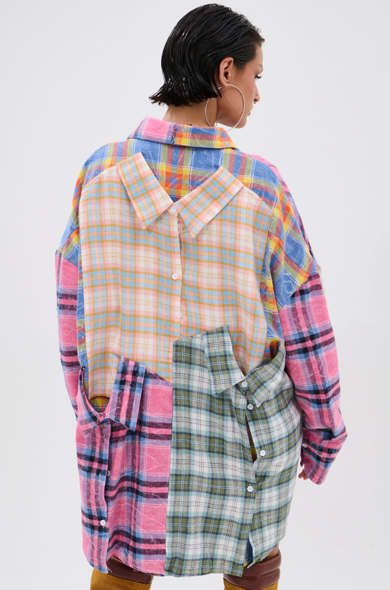 A person with short, wet hair wears the WILD CHILD PLAID SHIRT DRESS, an oversized, multicolored patchwork plaid shirt dress with visible back buttons. Facing away, they showcase the dress’s unique mixed-pattern design.
