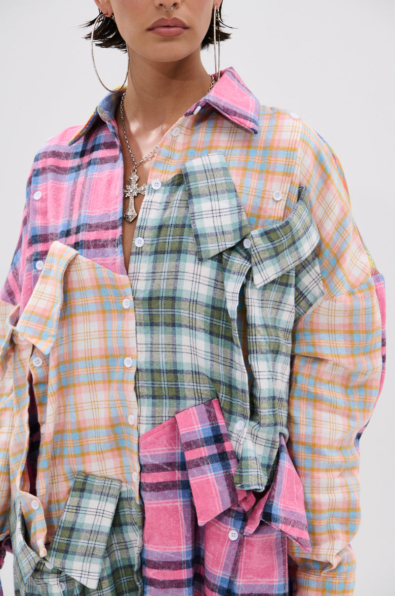 Wearing the WILD CHILD PLAID SHIRT DRESS with colorful patchwork plaid and oversized fit, accessorized with large hoop earrings and layered silver necklaces, the person stands against a plain white background.