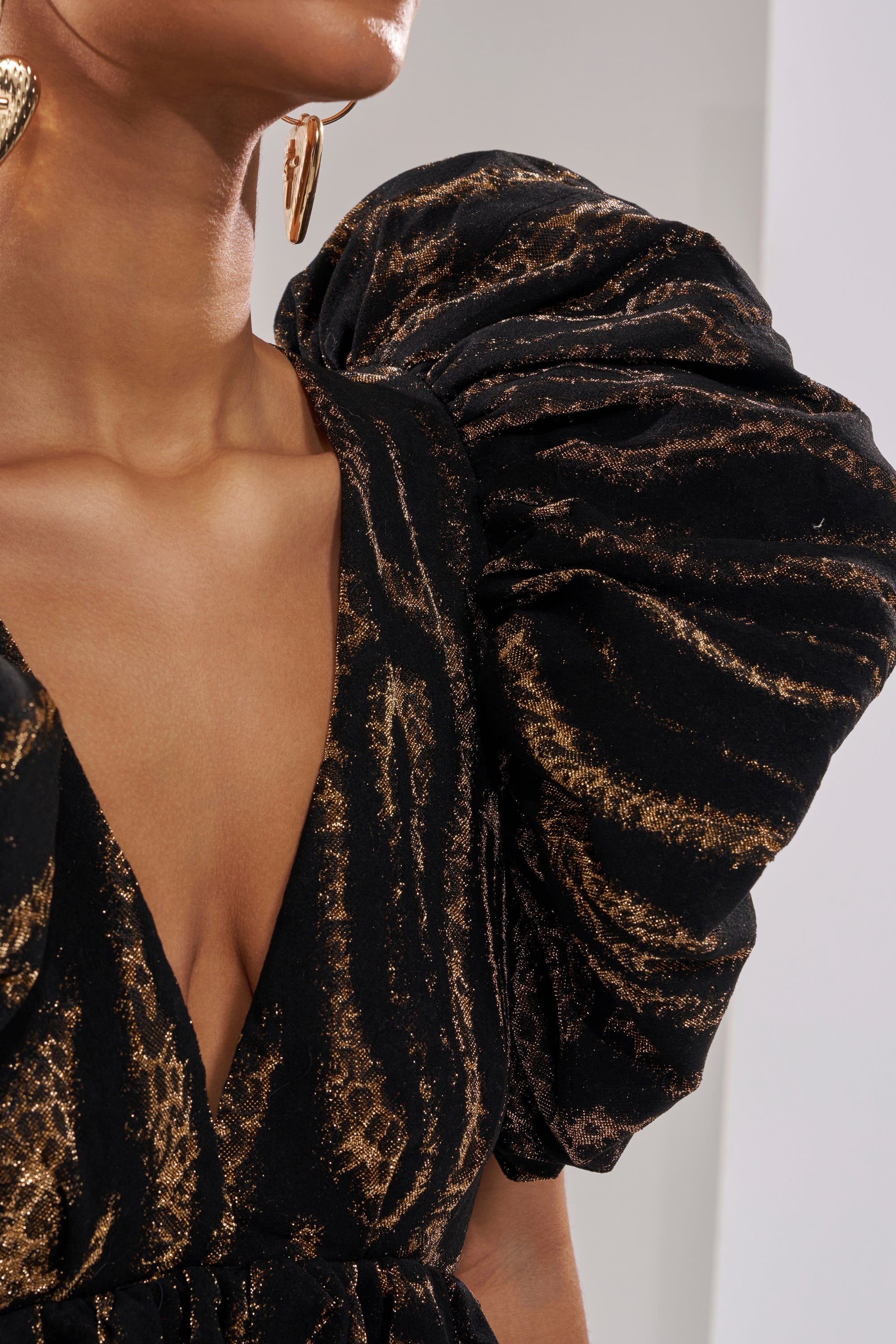 A person wearing the WILD HEART BROCADE BUBBLE MINI DRESS with puffed sleeves and a gold earring; only the neck, shoulder, and part of the chest are visible—perfect for a holiday party.