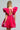 With braided hair, a person confidently showcases the BELLE OF THE BALL VELVET MINI DRESS, which features a vibrant pink color, puffed shoulder details, and an open back, standing against a simple background.