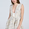 A woman wears the JUST A GIRL TWEED MINI DRESS IN WHITE with a sleeveless, plunging V-neckline and textured plaid. She poses against a plain background, holding a white handbag and wearing large hoop earrings with her long hair complementing the flared skater skirt.
