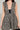 A woman is wearing the JUST A GIRL TWEED MINI DRESS, featuring a sleeveless, black and white checkered tweed design with a deep V-neckline. The dress is accentuated with gold details and textured fabric. Her head is not visible in the image as she holds a black handbag by her side.