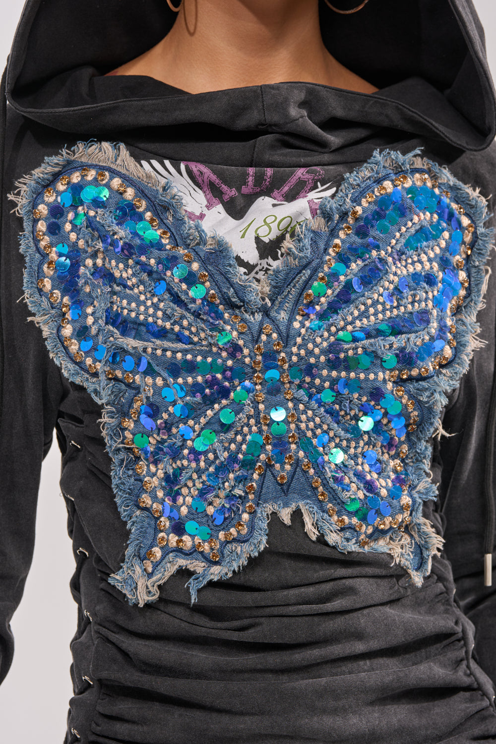The BUTTERFLY EFFECT MINI DRESS is a streetwear sweatshirt dress with a black hoodie, detailed with a large blue sequin and bead butterfly patch, frayed denim edges, and intricate embellishments. 9