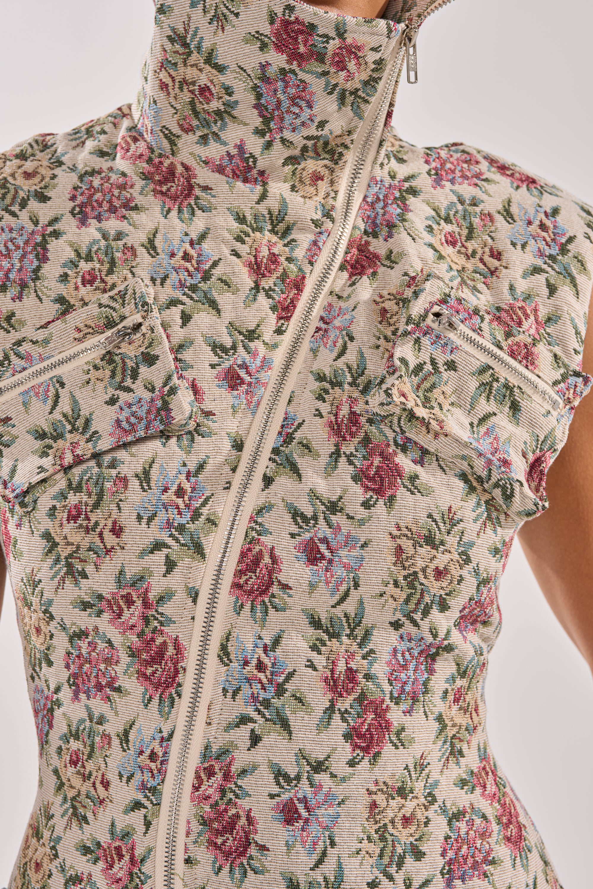 Close-up of the FLOWER POWER TAPESTRY MAXI DRESS, showcasing a beige jacquard floral print, sleeveless cut, high collar, off-center diagonal zipper, and two zippered chest pockets for added detail. 5