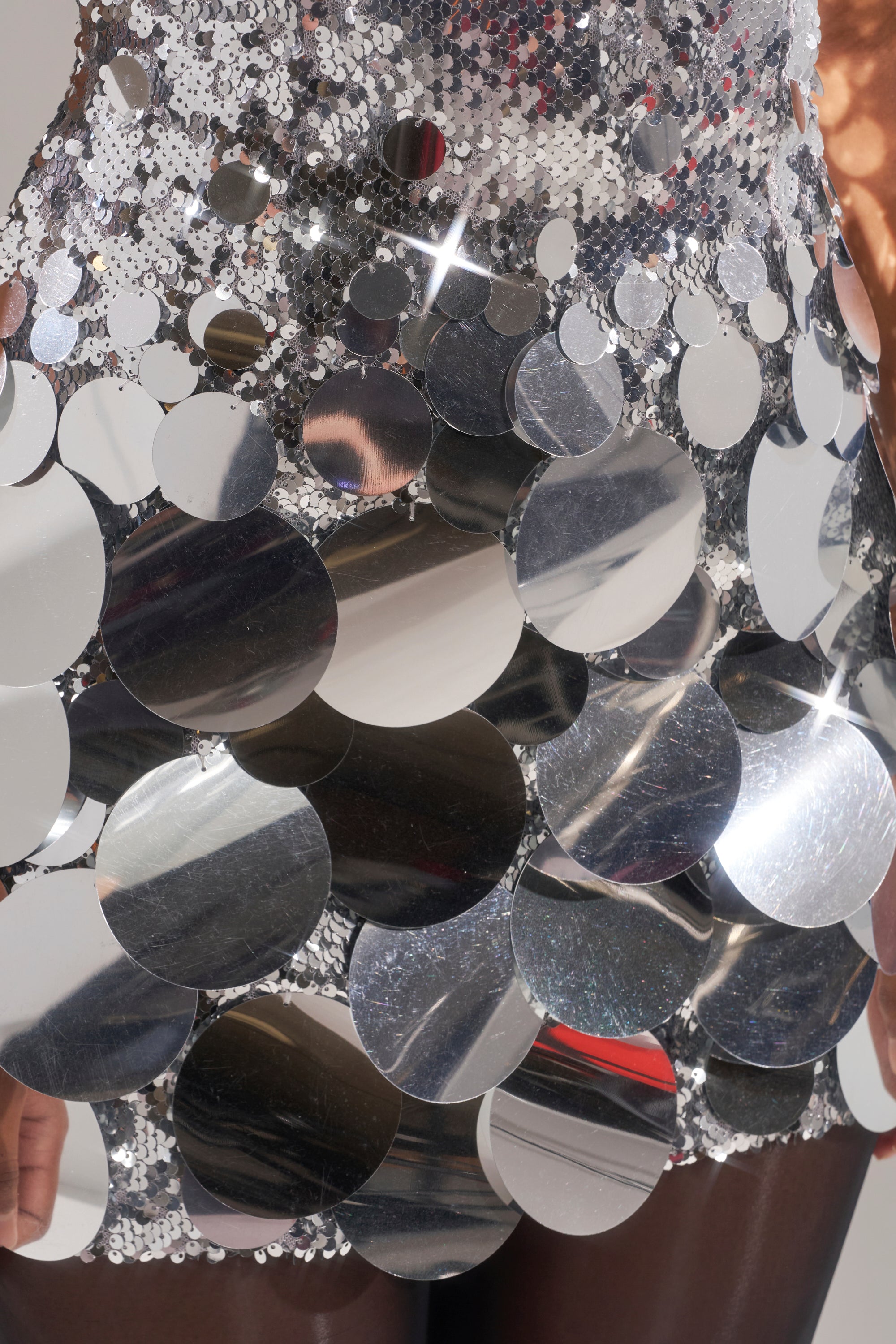 A close-up of the DANCE THE NIGHT AWAY SEQUIN MINI DRESS IN SILVER, featuring shiny sequins and large metallic circles that reflect light beautifully, with a softly blurred background.